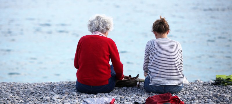Alte und junge Frau sitzen am Strand