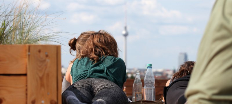 Junge Frau mit Getränken auf einer Dachterrasse mit Blick auf Berliner Fernsehturm